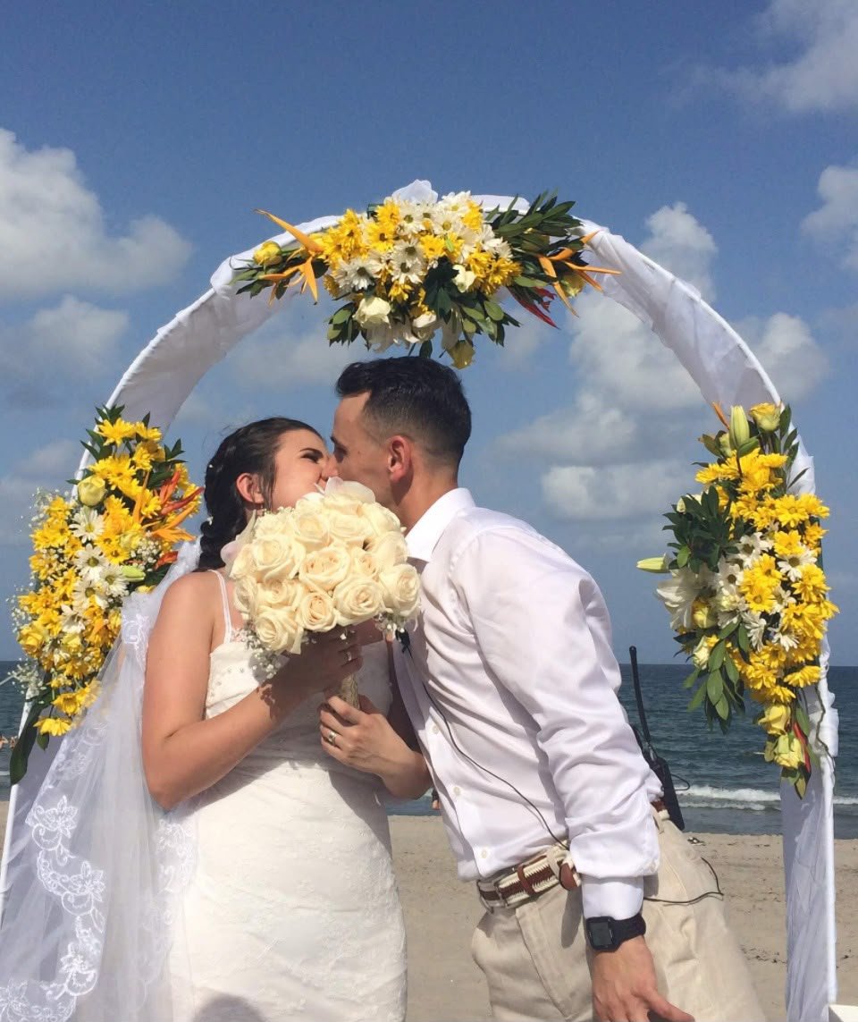 Couple kissing under a yellow floral beach arch